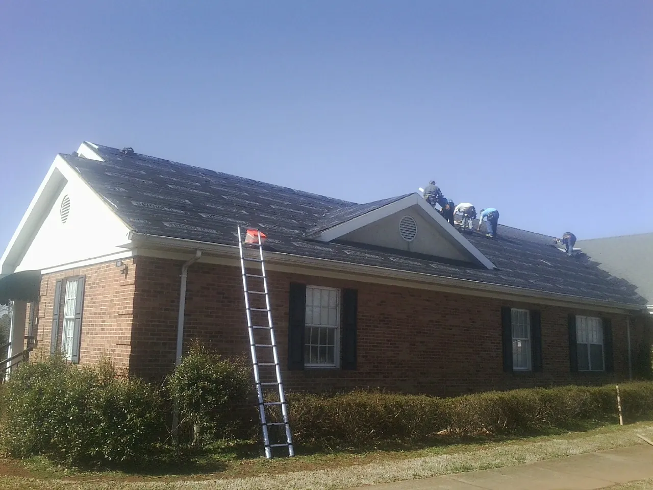 Crew tearing shingles off a brick ranch roof with a ladder set — Emergency Roof Repair work by our crew in Mapleton