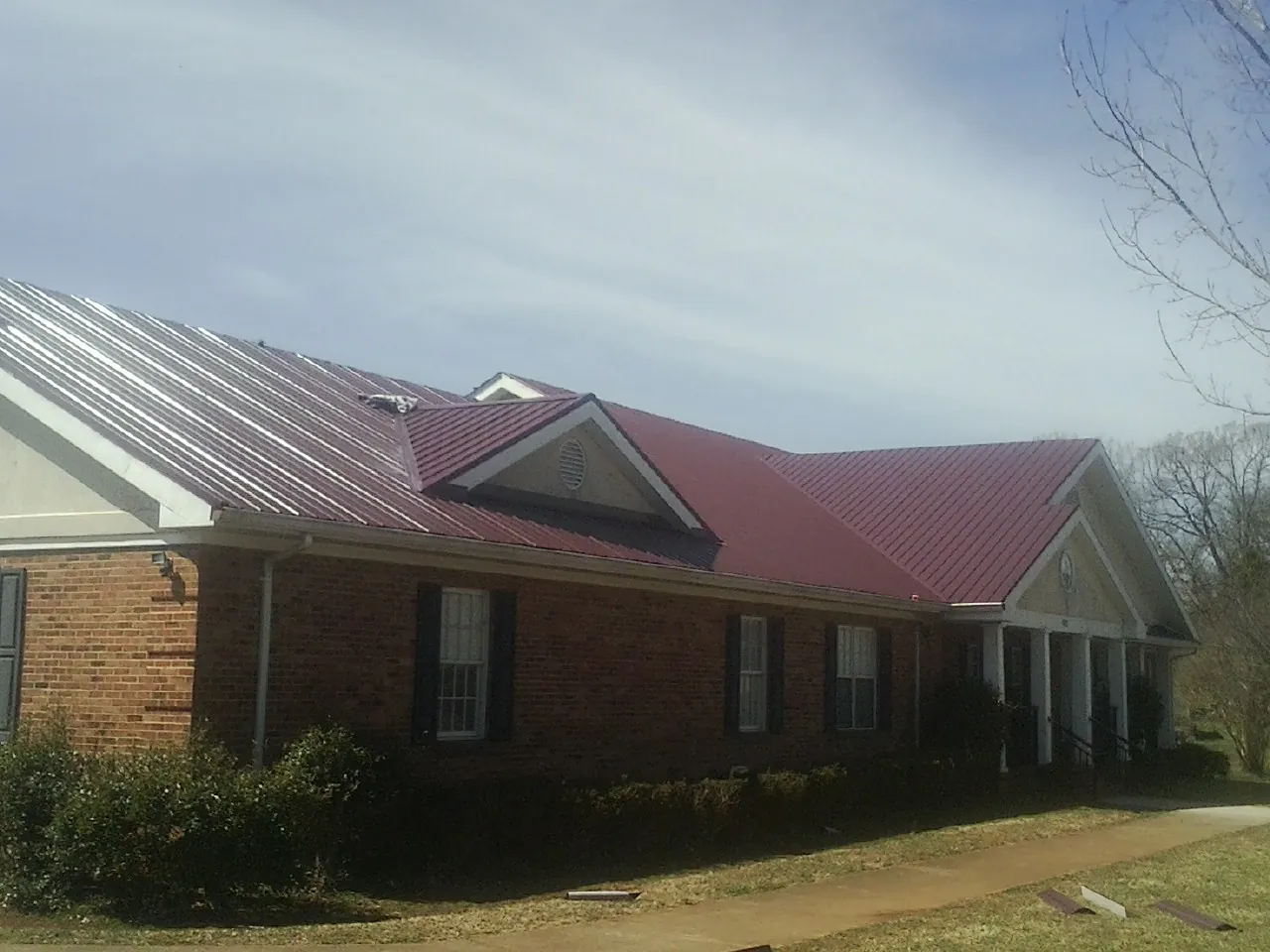 Red metal roof with gabled entries on a long brick building, from a Hail Damage Roof Repair job in Mapleton